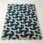 Angled view of the Coastal Mosaic rug featuring a geometric pattern of blue and beige semicircles arranged in a grid with scalloped edges.