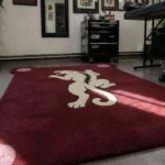 Low-angle view of the Crimson Prowl tufted novelty rug showcasing its plush wool pile, rich crimson tone, and unique corner details on a wood-look floor.