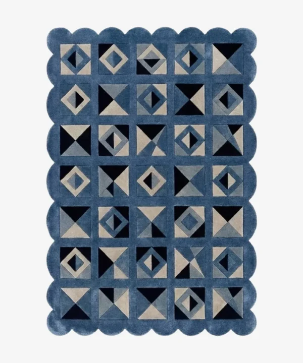 Top down view of the Indigo Tessellate rug against a white background, featuring a repeating patchwork pattern of geometric squares, triangles, and diamonds in solid shades of indigo blue, grey, and black, framed by a continuous blue scalloped border.