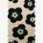 Top down flat lay of the Inked Botanica rug featuring bold black floral silhouettes with sage green centers on a beige wool background.