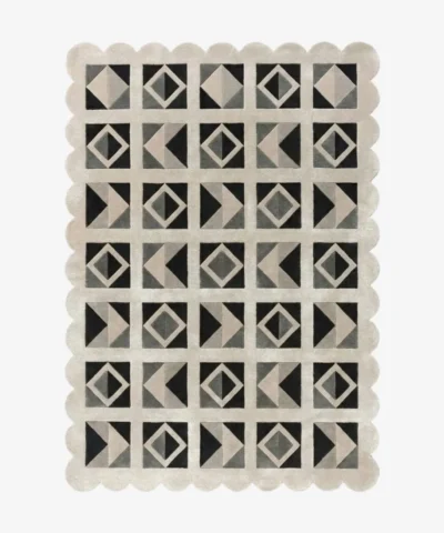 Top down view of the Shadow Grid rug against a white background, featuring a repeating patchwork pattern of geometric squares, triangles, and diamonds in shades of black, dark grey, light grey, and cream, framed by a continuous cream scalloped border.