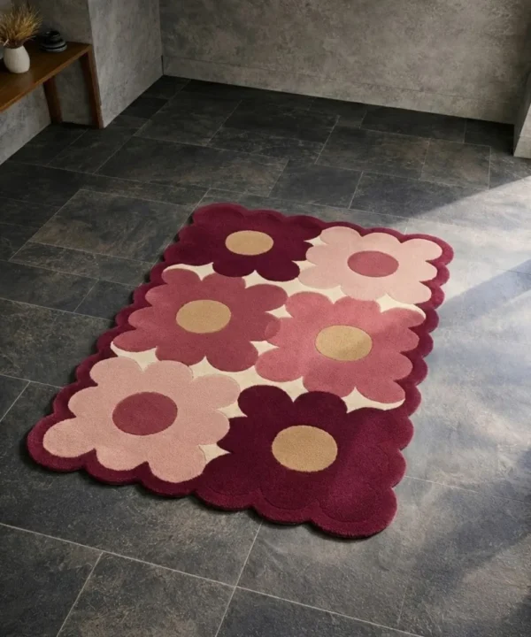 High angle view of the Velvet Garden rug placed on a dark tiled floor, featuring a retro large-scale floral pattern in shades of soft pink and deep burgundy with tan centers, finished with a unique scalloped edge that contours to the shape of the petals.