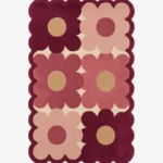 Top down view of the Velvet Garden rug featuring a playful grid pattern of large maroon and dusty pink flowers on a cream wool background, finished with custom scalloped edges.
