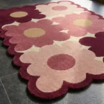 Close-up low angle view of the Velvet Garden rug, showcasing the plush hand-tufted wool texture, the embossed and deeply carved lines defining the overlapping flower petals, and the intricately contoured scalloped border.