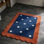 Perspective view of the Cosmic Constellation rug placed on a dark tiled floor, highlighting the deep navy blue center decorated with white stars and framed by a warm rust orange scalloped border.