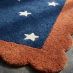 Close-up low angle view of the Cosmic Constellation rug, showcasing the plush hand-tufted wool texture, the embossed white star motif, and the intricately carved rust orange scalloped edge.
