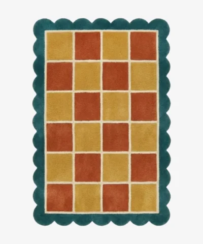 Top down view of the Sunbathe Quilt rug featuring a vibrant checkered pattern in rust orange, mustard yellow, and peach, framed by a cream line and a teal green scalloped border.