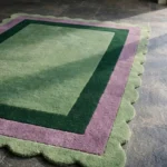 Close-up angled view of the Trimmed Forest rug, highlighting the plush hand-tufted New Zealand wool and viscose silk texture, the deeply carved lines separating the green and purple borders, and the intricately contoured scalloped edge.