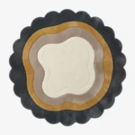 Top-down view of the circular Aurelith Flow rug, featuring a cream organic center surrounded by wavy concentric layers in soft taupe and mustard yellow, all framed by a thick, dark charcoal scalloped border.