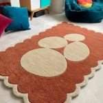 Perspective view of the Sienna Forms rug styled on a light carpet in a playful room setting, paired with bright pillows and a teal velvet beanbag chair to highlight its modern organic shapes.