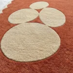 Close-up detail of the Sienna Forms rug, showcasing the plush hand-tufted wool cut pile and the crisp carving that defines the organic cream shapes against the textured rust orange background.