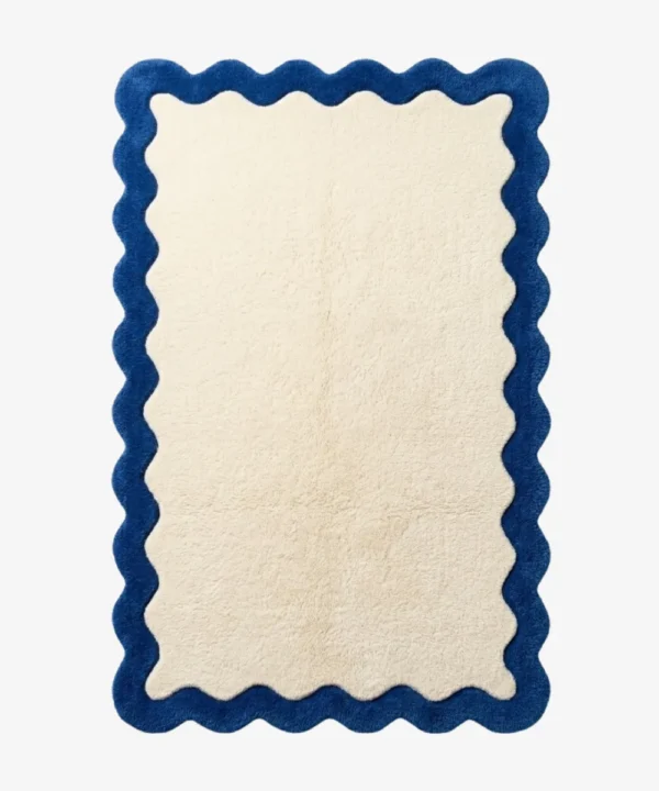 A top-down, flat view of the Azure Wave Scallop Rug on a clean white background. The tufted rug features a large rectangular cream center bordered by a thick, wavy, dark blue scalloped edge.