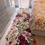 The Cassia Floral Runner Rug styled in a bright bedroom, laid on a light wood floor between a mirrored sliding wardrobe and a bed featuring a colorful polka-dot duvet. The rug's wavy, cut-out floral edges beautifully accent the narrow space.