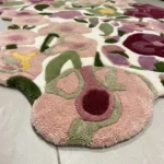 A close-up view of the edge of the Cassia Floral Runner Rug resting on a tiled floor. The image highlights the thick, hand-tufted yarn and the custom cut-out border that perfectly traces the natural shape of the pink and green floral design.