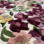 An extreme close-up of the Cassia Floral Runner Rug, showcasing the plush, high-quality tufted texture and varying pile heights. The depth and detail of the deep burgundy and soft pink flower blossoms are vividly displayed against the cream background.