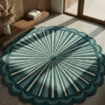 An angled overhead view of the Emerald Sunburst Round Rug placed on a smooth concrete floor in a sunlit modern room. The tufted circular rug features a radiating geometric sunburst pattern in shades of emerald green and cream, finished with a scalloped border.