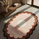 The oval Sunburst Flower Hand Tufted Wool Rug styled in a bright, modern minimalist room on a concrete floor. Bathed in natural sunlight next to a wood-slat wall and a floating wooden shelf, the rug showcases its bold, retro-inspired floral shape with concentric scalloped edges.