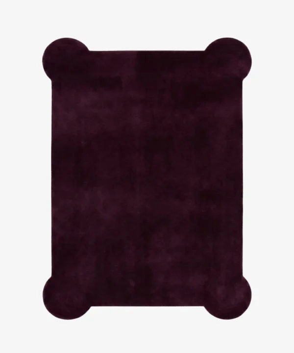 A flat, top-down view of the Bordeaux Scallop Rug isolated on a clean white background. The solid deep burgundy rug features a rectangular silhouette accented by unique, rounded scalloped corners and a rich, plush texture.