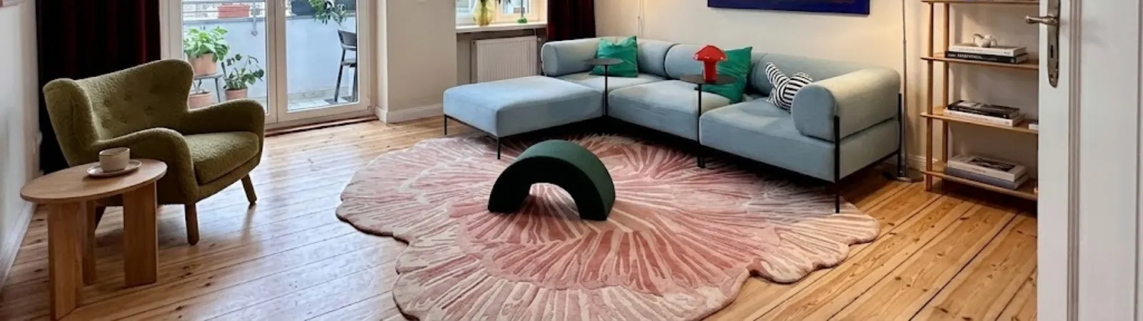 Wide view of a modern sunlit living room featuring a custom wavy green hand-tufted rug on a wooden floor, serving as the header image for the blog post 5 reasons hand tufted rugs are worth the investment.