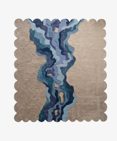 A flat, top-down view of the Lavelle Drift Rug isolated on a clean white background. The hand-tufted scalloped rug features a unique landscape-inspired design, showcasing carved topographical lines on a sandy beige base, intersected by a flowing, multi-colored blue and deep purple abstract river motif.