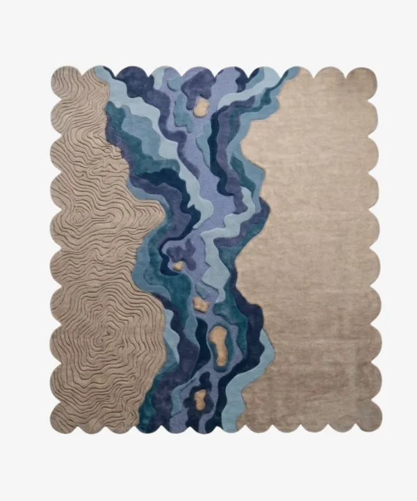 A flat, top-down view of the Lavelle Drift Rug isolated on a clean white background. The hand-tufted scalloped rug features a unique landscape-inspired design, showcasing carved topographical lines on a sandy beige base, intersected by a flowing, multi-colored blue and deep purple abstract river motif.