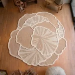 Overhead view of the Lunar Shell rug styled in a room with hardwood floors, featuring an organic, layered off-white floral design with textured tufting.