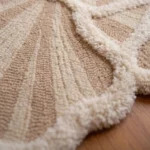 Close-up detail of the Lunar Shell rug on a wooden floor, highlighting the raised off-white scalloped edges and intricate ribbed hand-tufted texture.