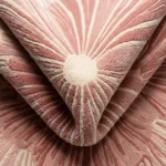 Close-up of the Rose Reverie rug folded, highlighting the intricate radiating lines, varying pile heights, and dense texture in shades of pink and cream.