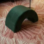 Detailed shot of a dark green velvet arch stool resting on the textured pink and cream surface of the Rose Reverie rug.