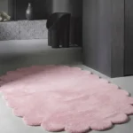 Wide angle shot of the oval Rosy Mellow Pink Scalloped rug on a clean, light-colored floor, creating a cozy and warm living space.