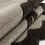 Extreme close-up of the Smokewood Mist rug folded, showcasing the thick hand-tufted plush pile and the clean visual transition between the off-white and dark gray yarn.