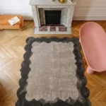 Smokewood Mist rug styled in a chic living room setting with a classic fireplace, chevron hardwood floors, and modern accent furniture.