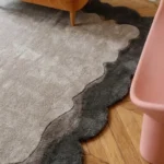 Close-up of the Smokewood Mist rug on a chevron wood floor, highlighting the organic wavy edges and the stark contrast between the off-white and dark gray sections.