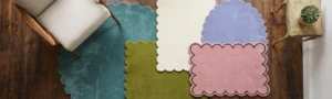 Overhead view of a collection of solid colored scalloped rugs in teal, olive green, cream, light blue, and pink, layered on a wooden floor to illustrate a solid rugs style guide.