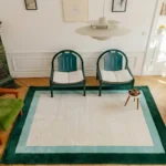 Overhead interior lifestyle shot of the Avelis border rug styled in a room with two green chairs and a modern pendant lamp.