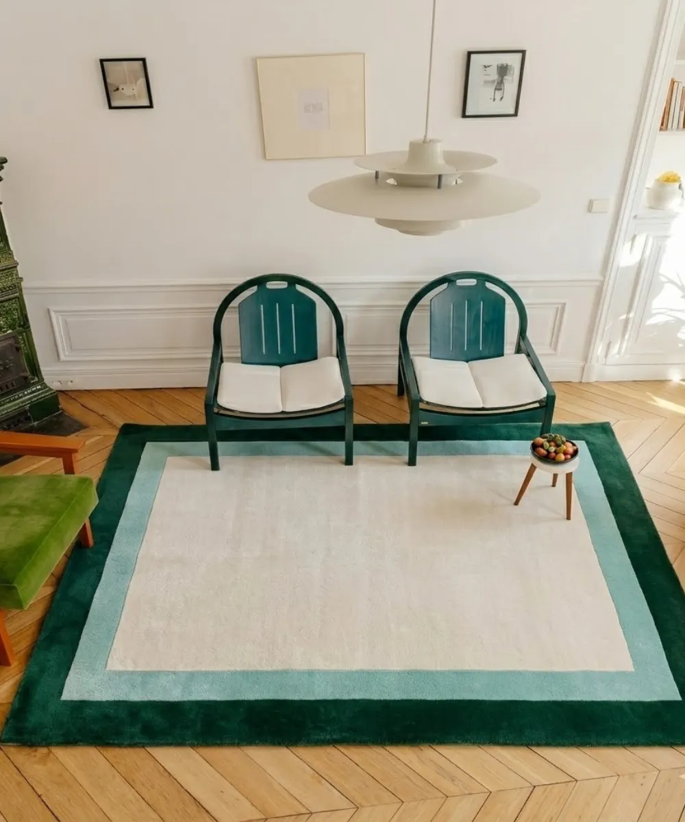 Overhead interior lifestyle shot of the Avelis border rug styled in a room with two green chairs and a modern pendant lamp.