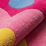 Close-up macro photograph showcasing the dense wool material loops, rich pile depth, and vibrant solid color blocks of the folded Bloomtopia floral rug.
