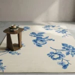 Wide perspective interior lifestyle view of the rectangular Bluevine Bloom traditional floral rug styled on a modern concrete gray floor next to a minimalist curved wooden side table.