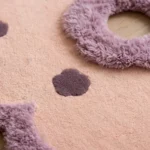 Close-up macro view of the Camellia Bloom rug, highlighting the plush, soft texture of its mauve scalloped border and deep purple floral details.