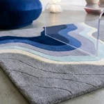 Low angle floor-level perspective showcasing the plush hand-tufted pile variations, precision-carved wave ridges, and vivid ocean blue gradient layers of the Coastal Meridian area rug.