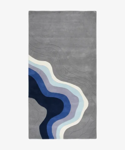 Full top-down product isolated shot of the rectangular Coastal Meridian area rug, featuring an intricate carved topographic wave design on a medium grey field transitioning into fluid abstract ocean contours of navy blue, royal blue, lavender, light teal, and cream.