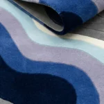 Close-up macro photograph highlighting the premium wool pile loops, rich tufted material quality, and layered solid color tracking of the folded Coastal Meridian rug.