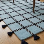 Low angle floor-level perspective showcasing the plush hand-tufted pile depth, crisp geometric line crossings, and dark navy fringe tassels of the Crosshatch area rug.