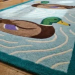 Low side-angle perspective shot showing the plush texture, teal border, and duck pattern of the runner rug.