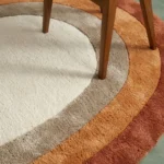 High-angle close-up floor view showcasing the precise hand-tufted pile divisions, carved organic curved borders, and distinct 1970s warm earth-toned color blocks of the Elio Bend accent rug.