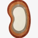 Full top-down product isolated shot of the custom kidney-bean-shaped Elio Bend accent rug, featuring concentric retro border rings in rust red, burnt orange, and taupe grey surrounding a solid ivory white center field.