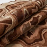 Close-up macro photograph highlighting the thick folded wool material and rich brown shades of the Ember Terrain rug.