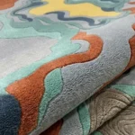 Close-up macro photograph highlighting the premium hand-tufted wool pile, thick material texture, and distinct organic fluid layers of the folded Estuary rug.