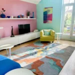Wide perspective interior lifestyle shot of the Estuary abstract landscape rug styled in a colorful modern living room with pink and mint walls.