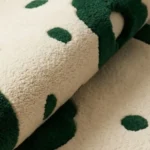 Close-up macro photograph highlighting the premium hand-tufted wool material texture, thick pile variations, and clean solid color blocks of the folded Fluera rug.
